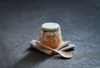 Sauerkraut with carrots and cumin in a jar on a linen napkin with a wooden spoon in a rustic style on a dark background