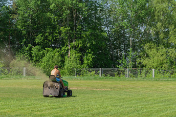 A man mows the grass with a lawn mower on a sports field
