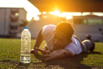 Thirsty man on grass at sport stadium reach for a bottle of pure water.
