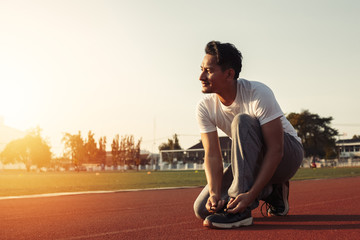 attractive brunette man tie him sport shoes on track race. A man at sport stadium with sunset.