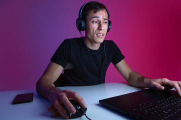 Gamer in headphones playing video games on computer in a dark room lit with neon lights.