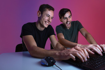 Two friends playing video game sitting in a dark room lit with neon lights. Video games championship