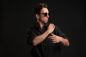 Confident stylish man in black eyeglasses fixing shirt isolated over black background.