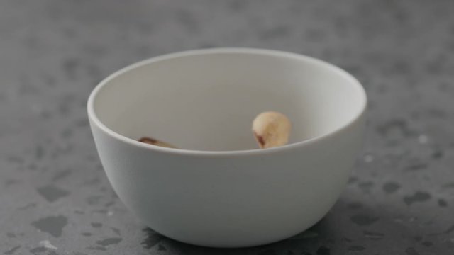 Slow motion brazil nuts falling into white bowl on terrazzo countertop