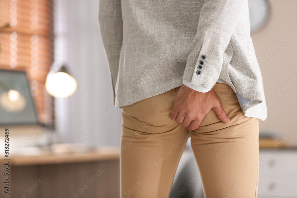 Wall mural Man suffering from hemorrhoid in office, closeup