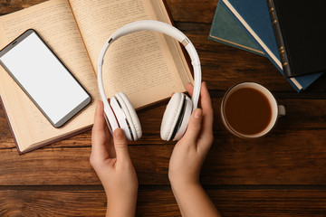 Woman holding headphones over wooden table with books, top view