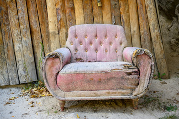 rosa Sofa Sessel verschlissen vor Holzwand auf Sandboden