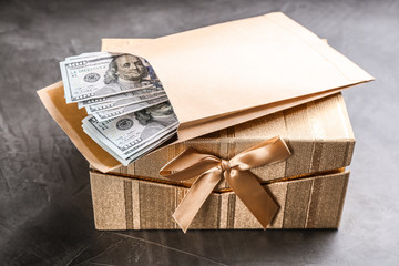Envelope with dollar bills and gift box on grey stone table