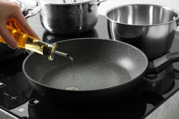 Woman pouring cooking oil from bottle into frying pan, closeup