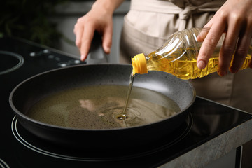Woman pouring cooking oil from bottle into frying pan, closeup