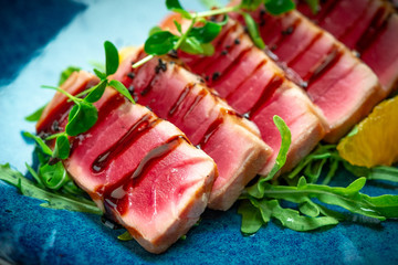 Sliced grilled tuna with green salad and tomatoes in a plate on a wooden background. Close up