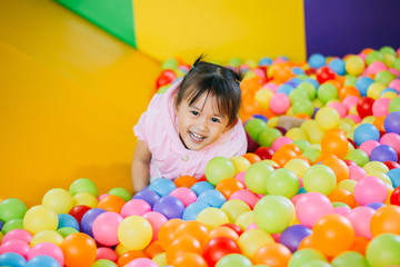 Fototapeta na wymiar Smiling baby playing in the balls pool. Cute and happy girl. Picture for developmental in children concept.