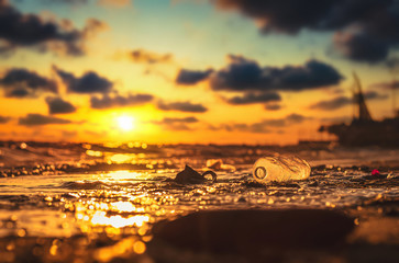 Plastic water bottle on the beach, environment pollution. Dirty beach and sunset.