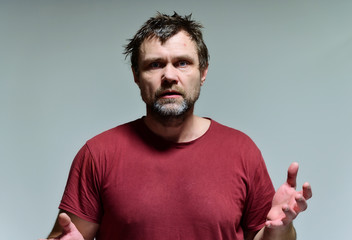 Portrait of a wild unkempt unshaven middle-aged man of 40 years in a burgundy t-shirt on a gray...