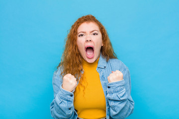 young red head woman shouting aggressively with annoyed, frustrated, angry look and tight fists,...