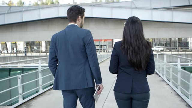 Back view of business colleagues walking on street. Rear view of young businessman and businesswoman in formal wear walking together on street and discussing work. Business concept