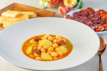 Hot soup sauce with sausages, potatoes and soybeans in the white dish, on the table served also with cheese sticks and sausage salami.