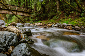 Water flows under a bridge and around large rocks at Sonoma Creek in Sugarloaf Ridge State park in Kenwood California