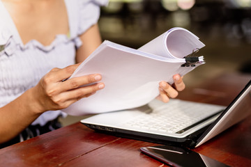 woman opening and reading a paper sheet near laptop on wooden table.