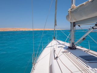 Sailing boat slowly moving on a crystal blue sea towards an island