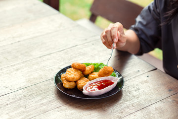 Chicken Nuggets impaled on a fork  and Dip sauce. A women eat Nuggets.
