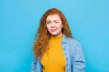 young red head woman looking happy and friendly, smiling and winking an eye at you with a positive...