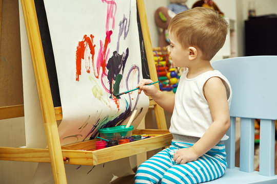 little boy paints a on an easel