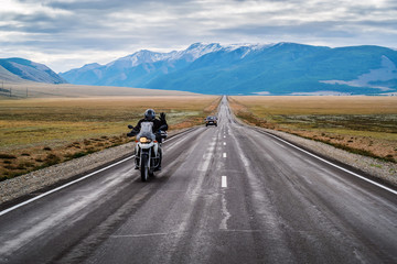 A motorcyclist with his hand raised in greeting, riding along the Chuysky highway at dawn, landscape with a highway. Russia, mountain Altai