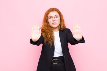 young red head woman looking serious, unhappy, angry and displeased forbidding entry or saying stop...