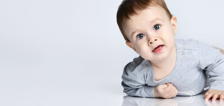 Portrait of little baby boy toddler in grey casual jumpsuit lying on floor and smiling over white wall background
