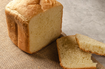Wheat bread, white. On the table lies a loaf of white bread, slices of bread. Close-up.