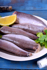 Fresh raw carcass of hake, greenery and lemon on the white plate. Ingredients for a fish dish