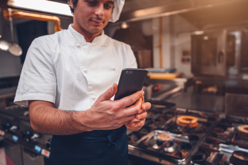 Caucasian man chef working in the kitchen and using a smartphone
