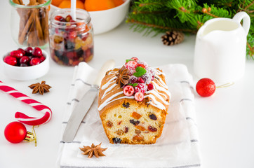 Traditional fruit cake with mixed fruit and cherries decorated with sugar icing, cranberries, pomegranate and cherry on a white background. Horizontal orientation.