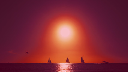Fototapeta na wymiar Scarlet sails against the backdrop of a red sunset, view from a tropical beach. Sea sunset landscape. Twilight over the ocean with yachts. Cuban coastal zone. Evening over the sea.