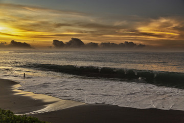 A boy by the sea. A large wave rolls onto a sandy beach. Colorful sunset in Tahiti.