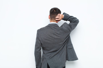 young handsome man thinking or doubting, scratching head, feeling puzzled and confused, back or...