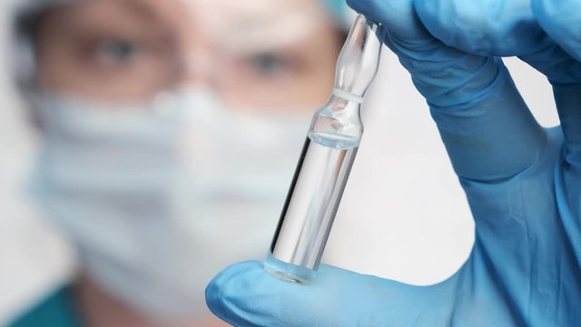 Glass ampoule with medicine in hands of doctor close-up, blurred background. concept of vaccination during an influenza epidemic.
