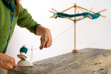 caucasian woman working a hand-operated knitting roll to prepare wool thread for knitting