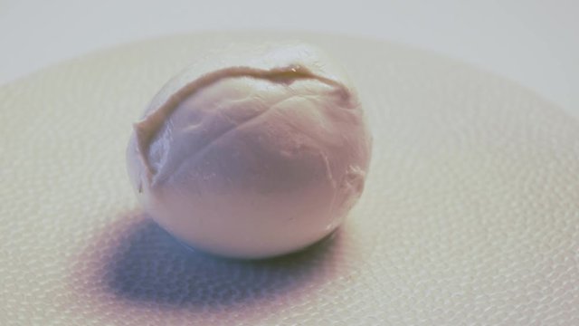 Soft white italian mozzarella cheese rotating on white plate