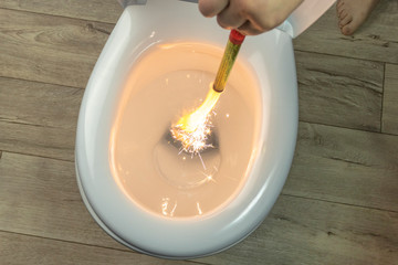white toilet bowl on a wooden background. the hand lowers the lit firecracker. close-up.