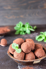 Dark chocolate truffles candy with raw cocoa powder and mint in a wooden bowl, dark brown stone background. 