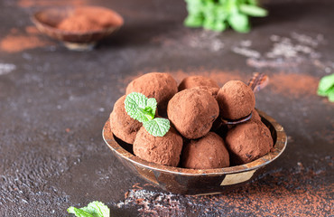 Dark chocolate truffles candy with raw cocoa powder and mint in a wooden bowl, dark brown stone background. 