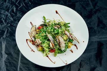 Gourmet salad served with roasted sea bass, spinach, lettuce, cherry tomatoes on black background. Delicious seafood salad. Healthy food. Diet and fitness nutrition