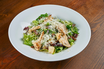 Caesar salad with croutons, parmesan, chicken, egg in a white stylish bowl. Restaurant serving. Selective focus, wooden background
