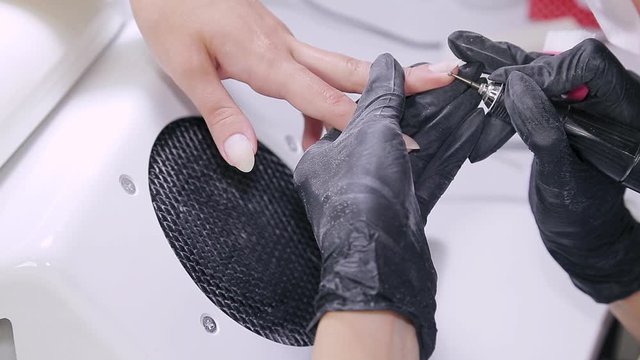 Manicurist woman in gloves in the beauty salon processes the cuticle on the nails of the client. overall plan