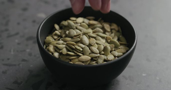 Slow motion closeup of man hand takes pumpkin seeds from black bowl