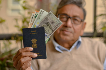 Portrait shot of an Indian senior citizen holding his passport with some dollar bills in it, face blurred. Concept shot depicting global traveler or first generation immigrant