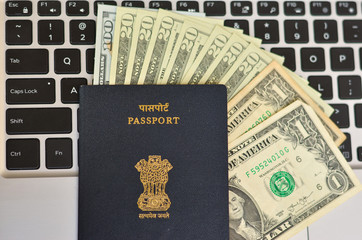 Indian Passport kept against a laptop keyboard and dollar bills, foreign currency.  National emblem, Lion Capital of Ashoka from Sarnath is embossed. Concept Wealthy IT professional Global citizen