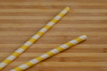 Abstract shot of a couple of Yellow and white striped Straws made with recyclable paper arranged neatly on a wooden background. Concept - Ban plastic and save enviornment